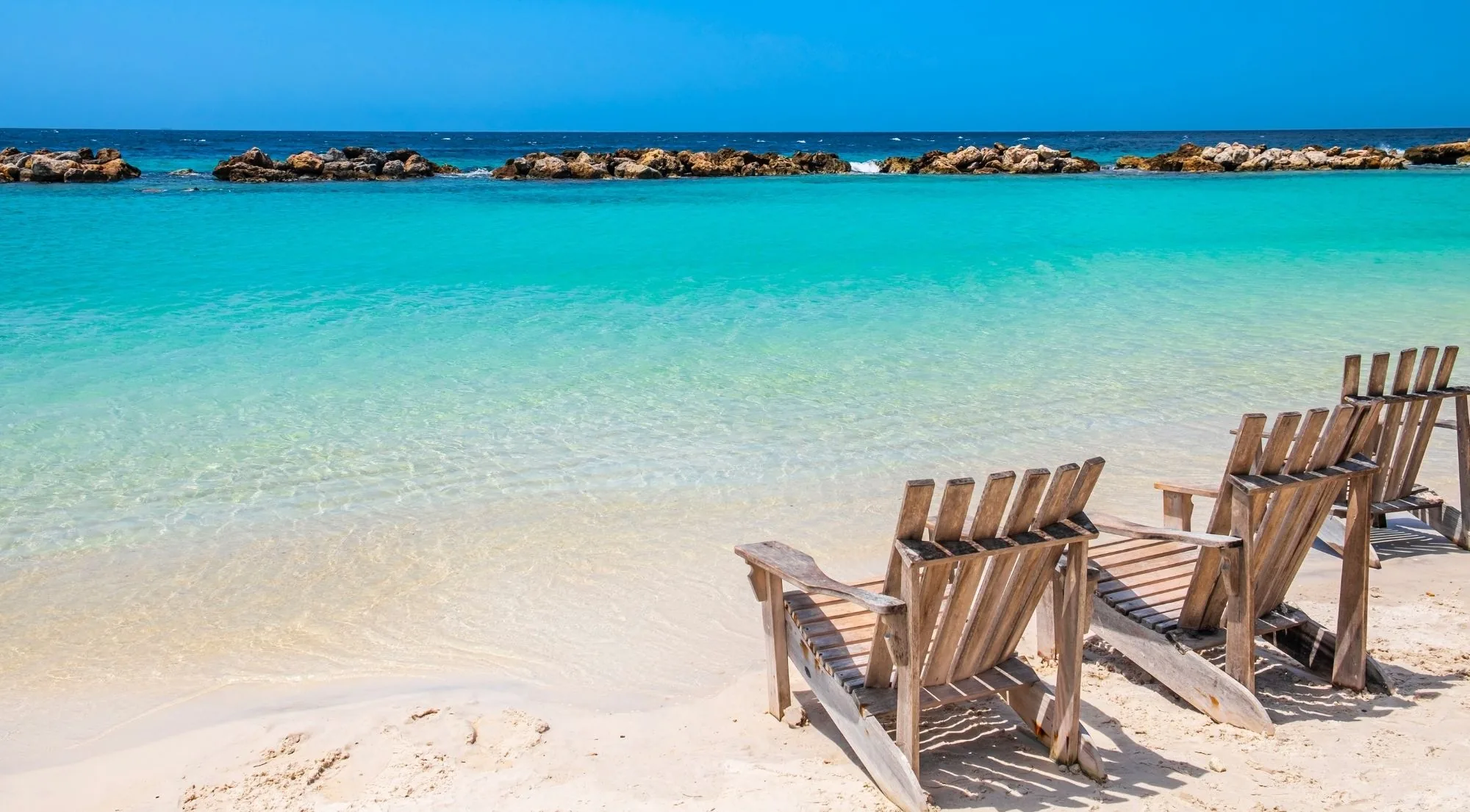 Wooden deck chairs at the waterline of a sheltered turquoise Curaçao bay
