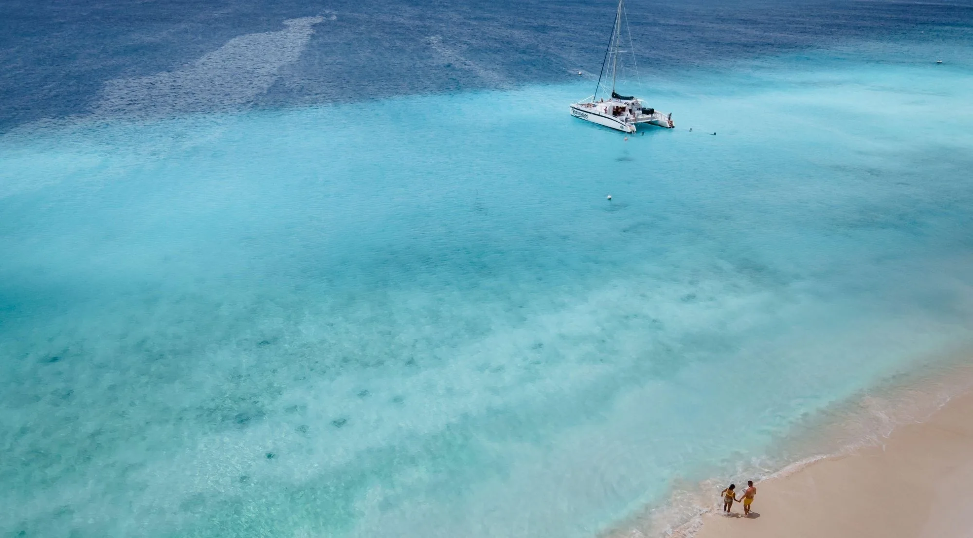 Aerial view of a catamaran anchored in turquoise shallows off Klein Curaçao's white sand beach