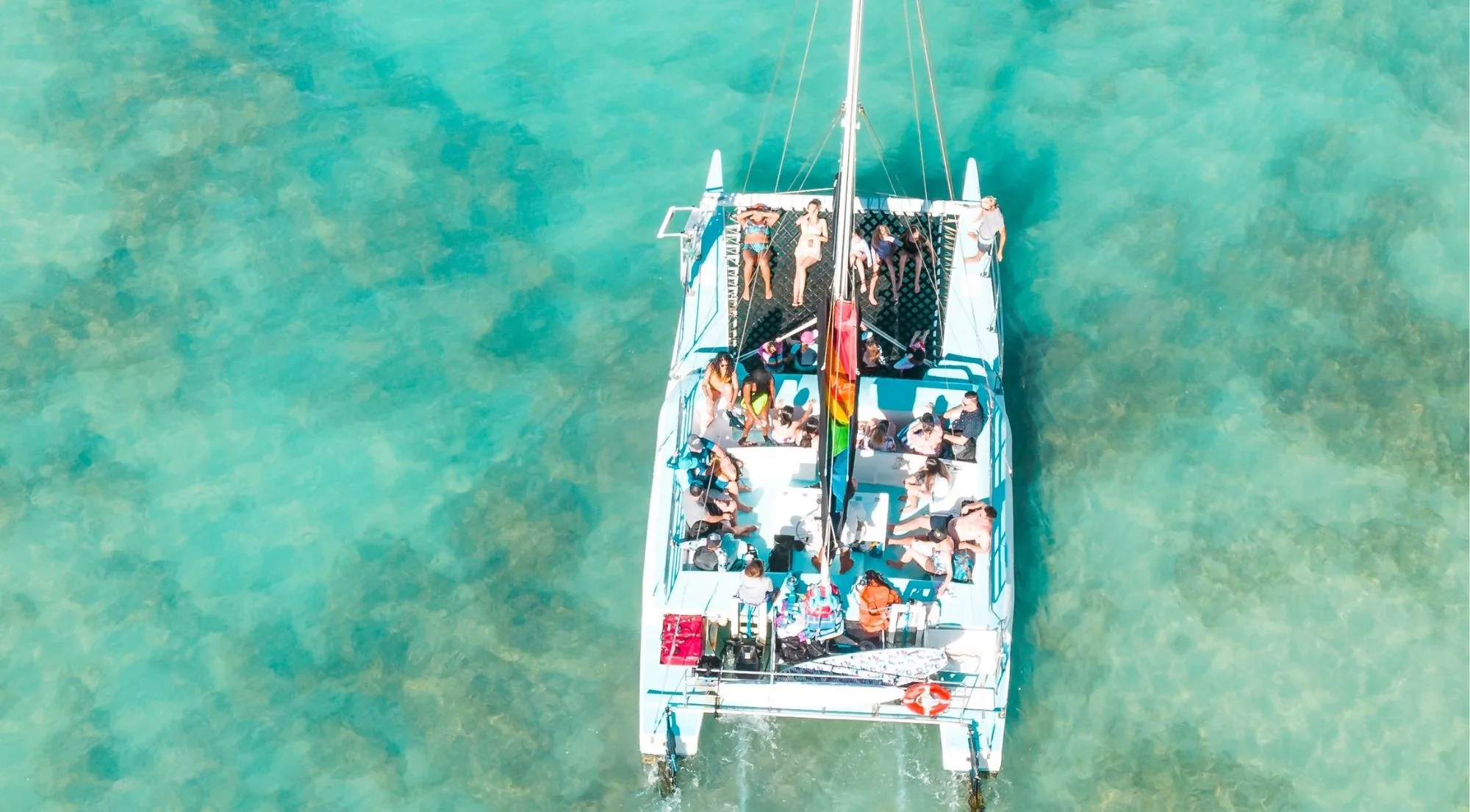 Aerial view of a full catamaran deck on the crossing to Klein Curaçao, passengers spread across the trampoline and cockpit