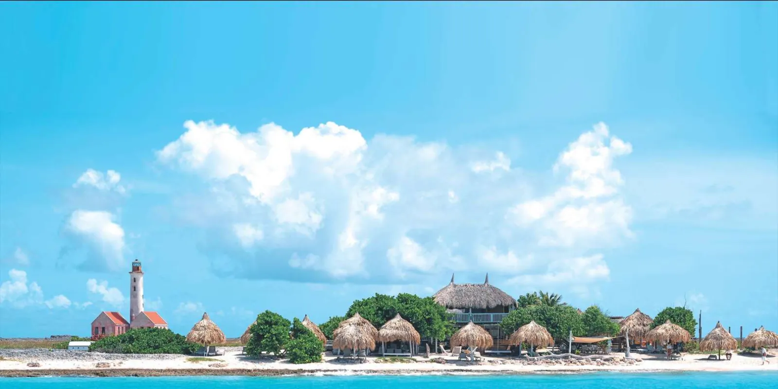 Klein Curacao's pink lighthouse and the row of beach-house palapas seen from the water