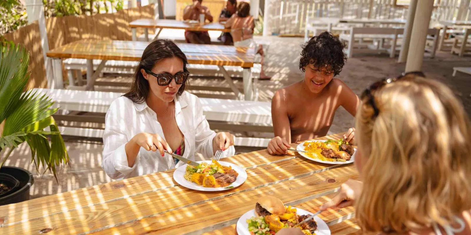 Guests eating the barbecue lunch at the beach house's long wooden tables